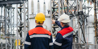 Two utility engineers inspecting modern high-voltage equipment at an electrical station.